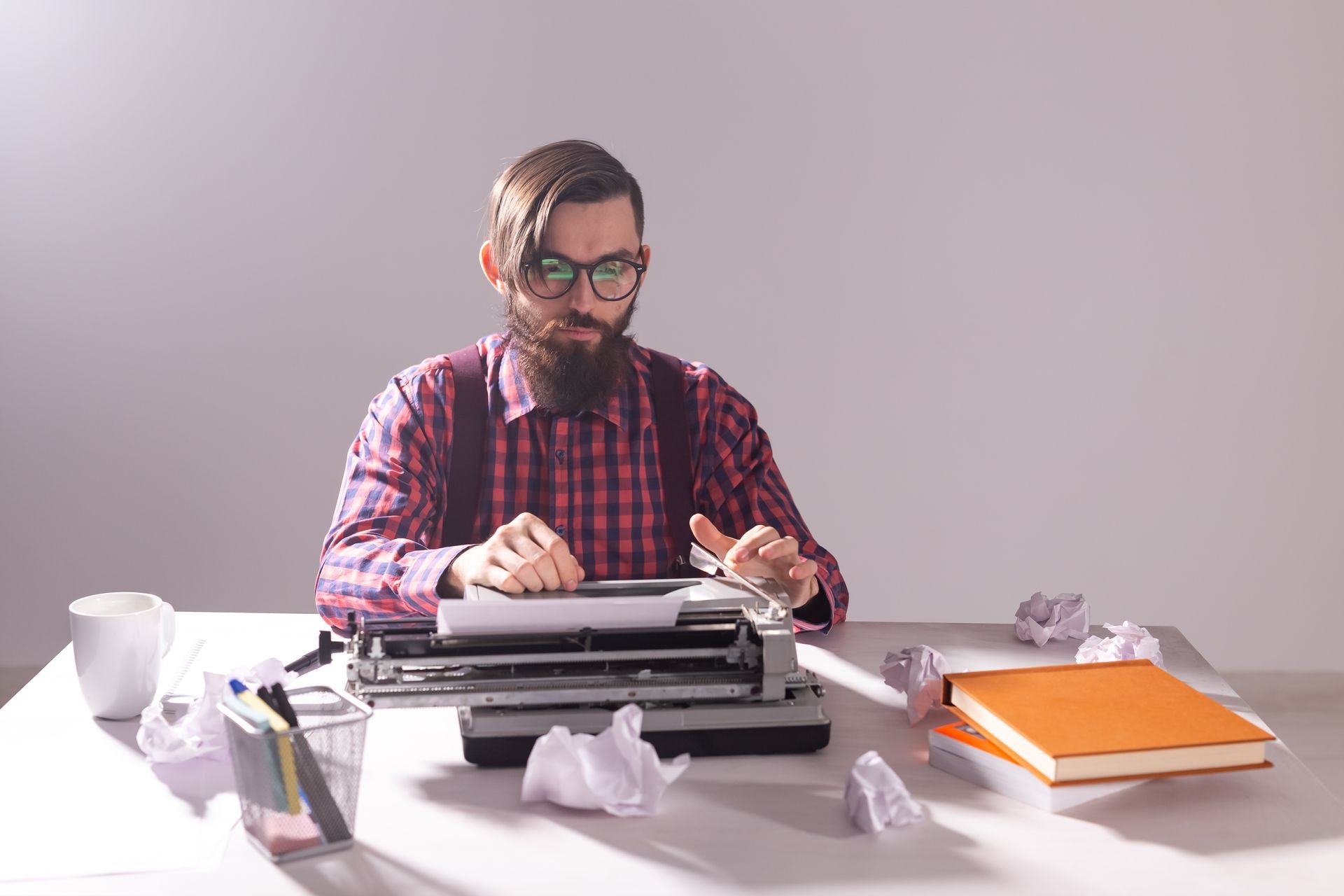 Writer's day and technology concept - Handsome writer surrounded by scraps of paper focused on work over grey background
